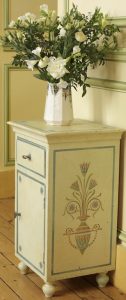 MEUBLE PEINT : Sur une armoire chevet, composition de motifs au pochoir cernés de filets bleus sur une patines blonde.